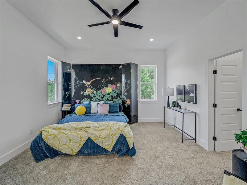 Bedroom with light colored carpet, multiple windows, and ceiling fan