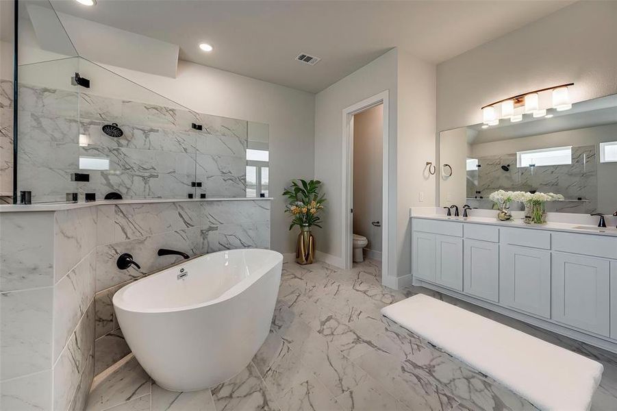 Full bathroom with a freestanding tub, walk in shower, toilet, marble finish floor, and a sink