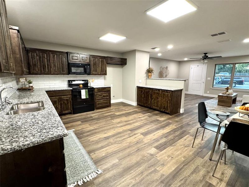 Kitchen featuring dark brown cabinets, black appliances, light stone counters, decorative backsplash, and ceiling fan