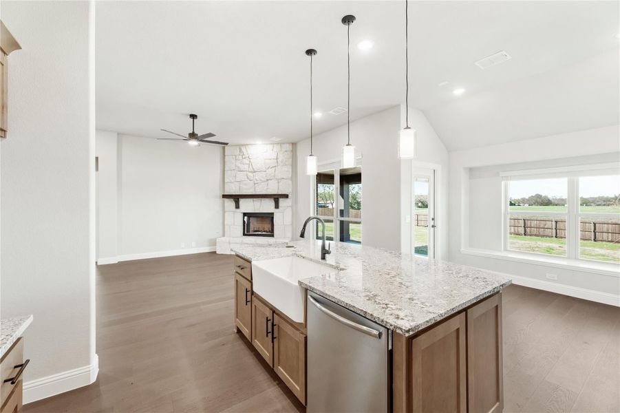 Kitchen island with granite countertop and farmhouse sink, open to living room with stone fireplace and hardwood floors Kitchen island with granite countertop and farmhouse sink, open to living room with stone fireplace and hardwood floors
