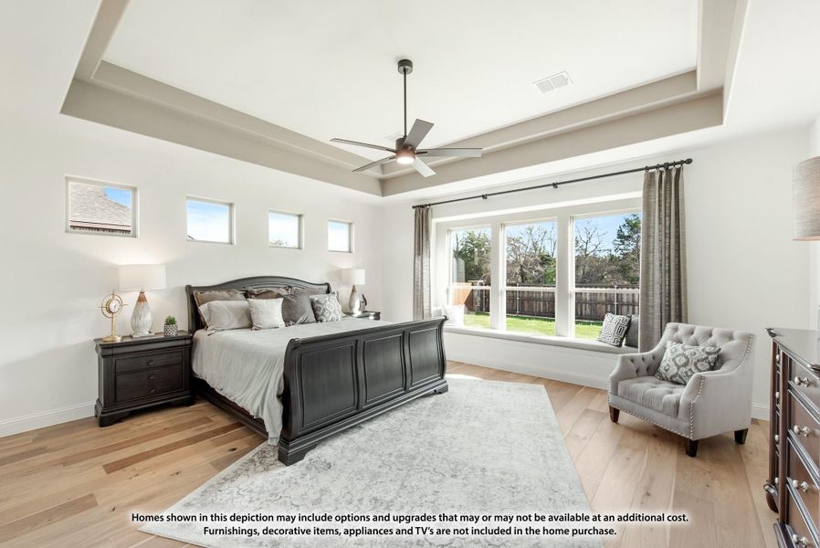 Master bedroom with tray ceiling, ceiling fan, dark wood sleigh bed, hardwood floors, and large windows with window seat.