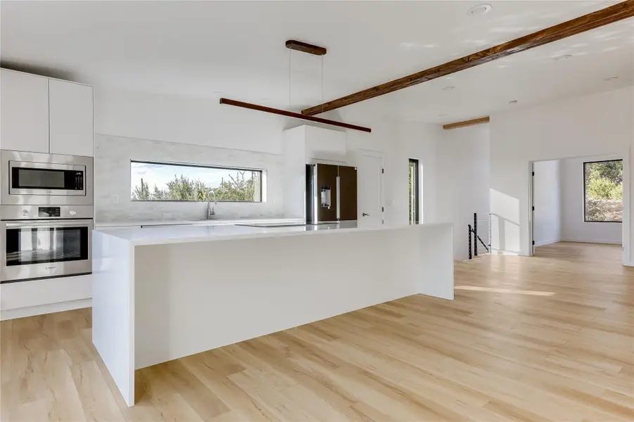 Kitchen with appliances with stainless steel finishes, white cabinetry, a spacious island, modern cabinets, and light wood-style flooring Kitchen with appliances with stainless steel finishes, white cabinetry, a spacious island, modern cabinets, and light wood-style flooring