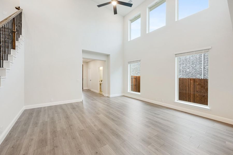 Open living room with two-story ceiling, hardwood floors, ceiling fan, and large windows near staircase