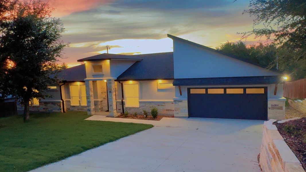 Modern home with stone siding, driveway, a garage, stucco siding, and a yard