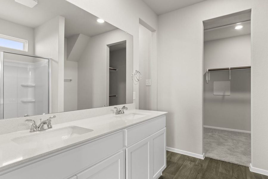 Image of primary bathroom with white cabinets and vanity with a mirror and a connected walk in closet