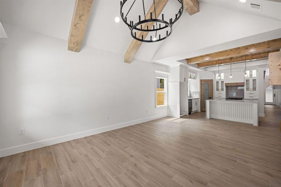 Spacious open-concept living area featuring a vaulted ceiling with exposed wood beams and a large circular chandelier