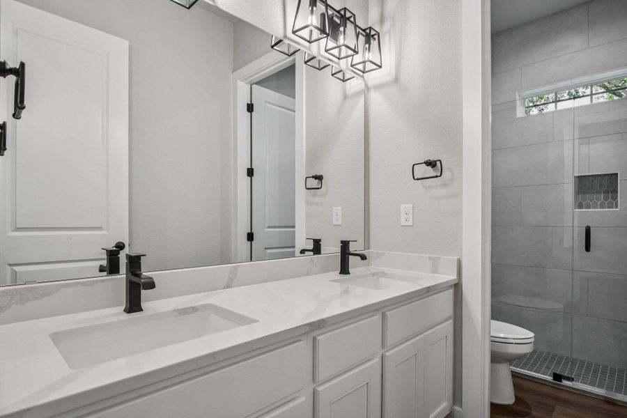 Full bath with double vanity, dark wood-style flooring, and a shower stall