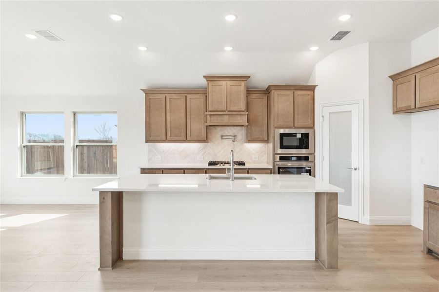 Kitchen with large white island, tan wood cabinets, tile backsplash, and stainless steel appliances Kitchen with large white island, tan wood cabinets, tile backsplash, and stainless steel appliances