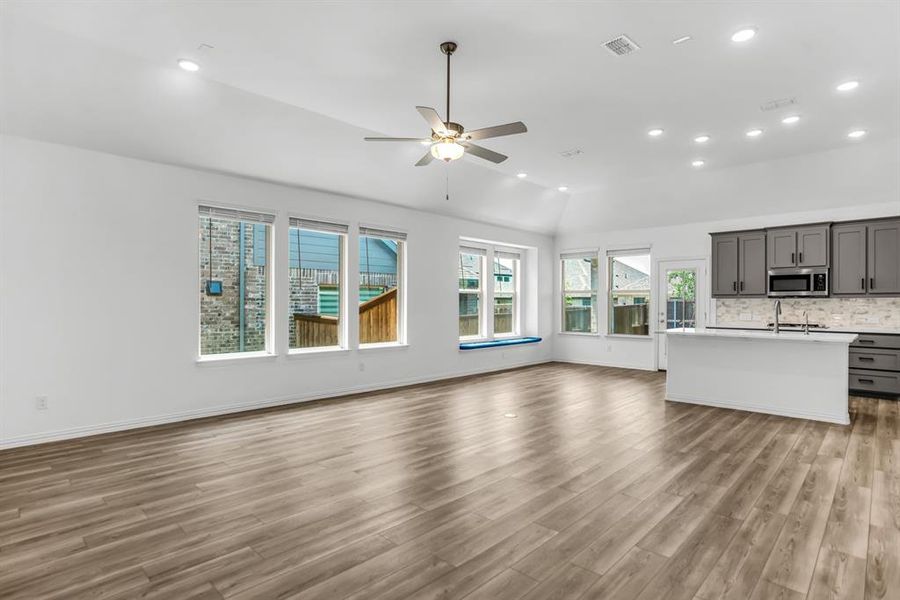 Spacious open-concept living area featuring wood-finish flooring, vaulted ceilings, and recessed lighting