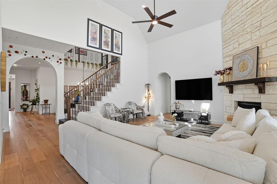 Living room featuring arched walkways, hardwood / wood-style floors, high vaulted ceiling, a fireplace, and stairway