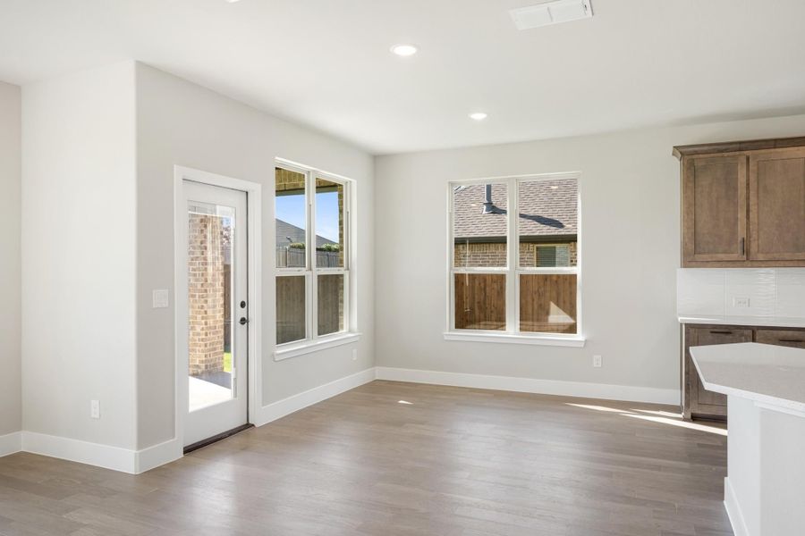 Bright dining area with hardwood floors, back door, and two windows next to kitchen cabinets