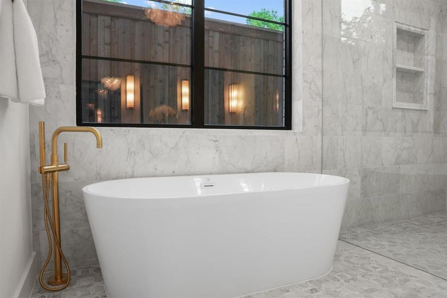 Bathroom featuring a freestanding soaking tub with a floor-mounted golden faucet, a tiled floor, and a tiled accent wall