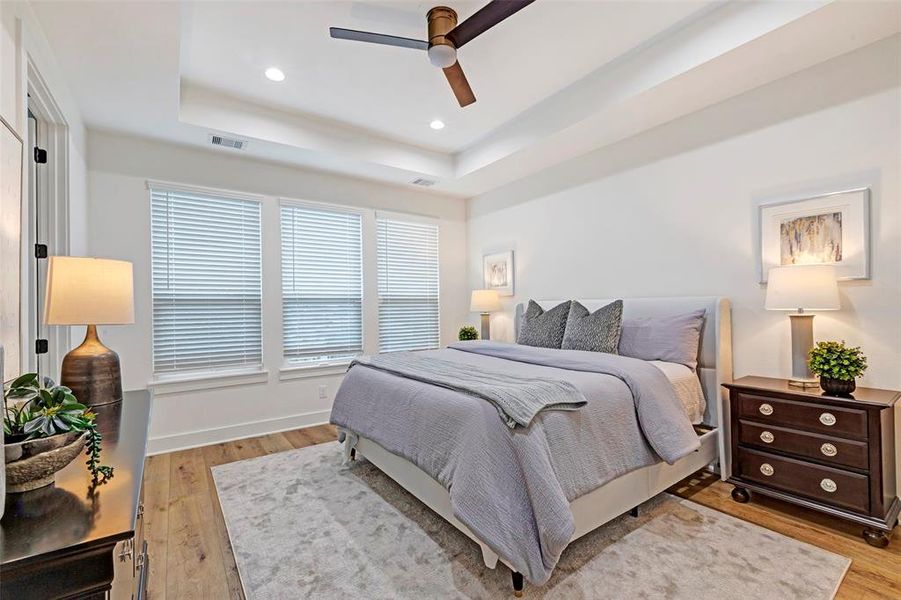 Your primary bedroom offers a great place to relax after a long day. Enjoy the wood floors, tray ceiling, and ceiling fan, plus natural light from the windows.