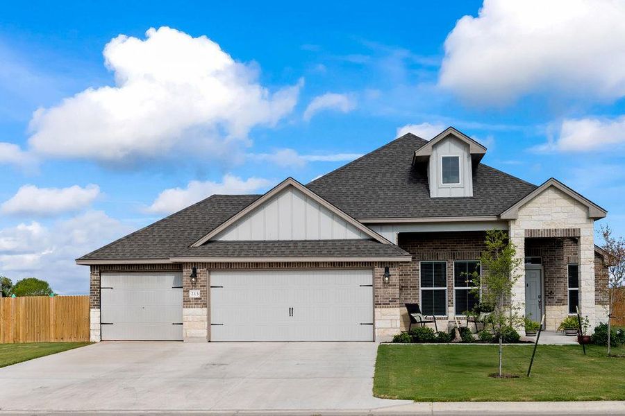 View of front of home with a shingled roof, an attached garage, brick siding, stone siding, and board and batten siding