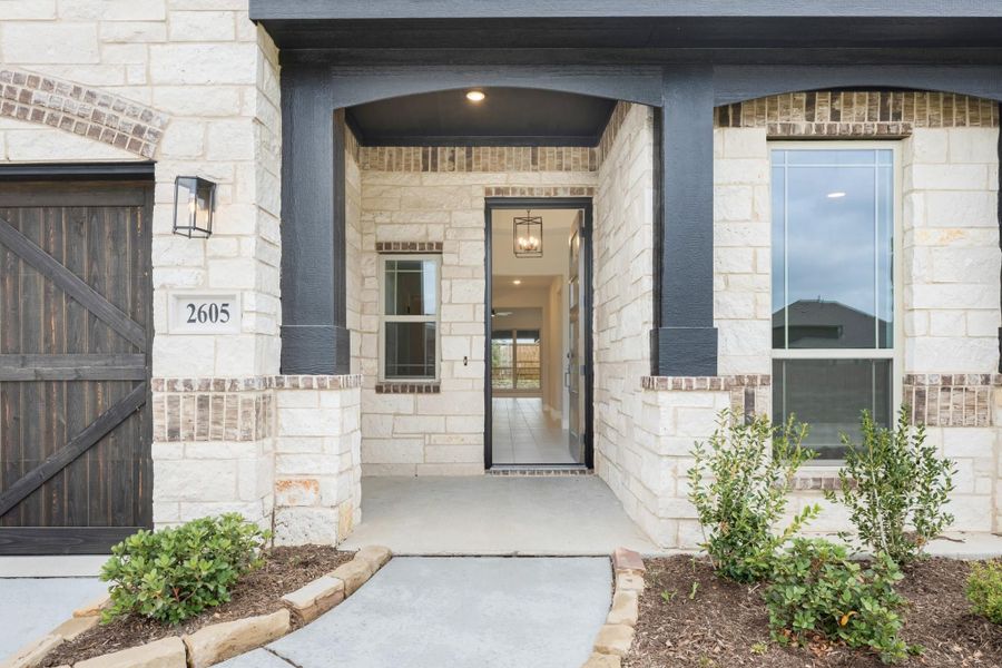Home entrance with stone exterior, arched covered porch, dark front door, and pendant light at address 2605 Home entrance with stone exterior, arched covered porch, dark front door, and pendant light at address 2605