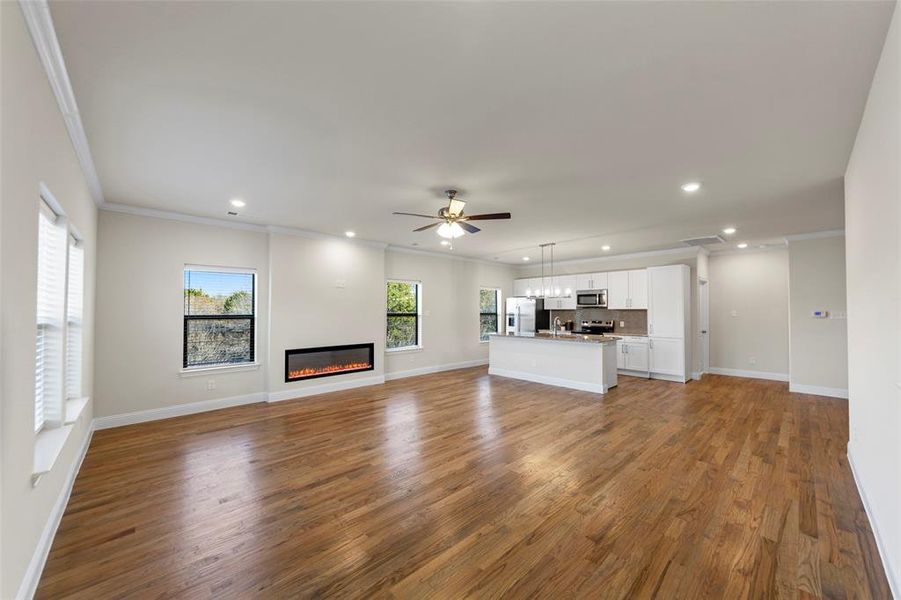 Unfurnished living room with dark wood-type flooring, crown molding, ceiling fan, a glass covered fireplace, and recessed lighting