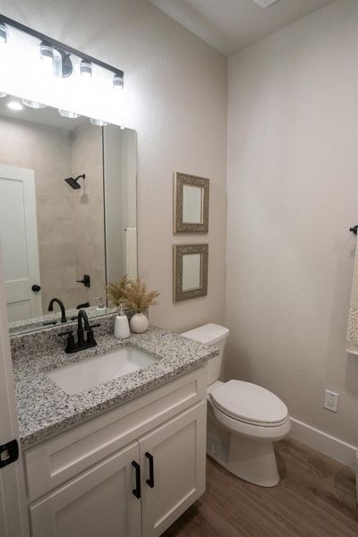 Bathroom featuring vanity, wood finished floors, toilet, a tile shower, and baseboards