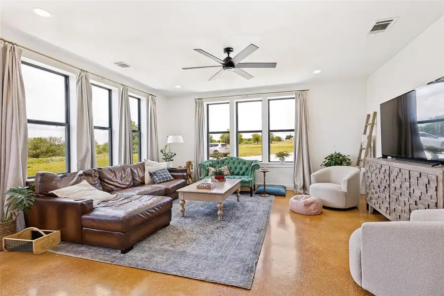 Spacious living area featuring polished concrete flooring, multiple large windows, a ceiling fan, recessed lighting, and crown molding Spacious living area featuring polished concrete flooring, multiple large windows, a ceiling fan, recessed lighting, and crown molding