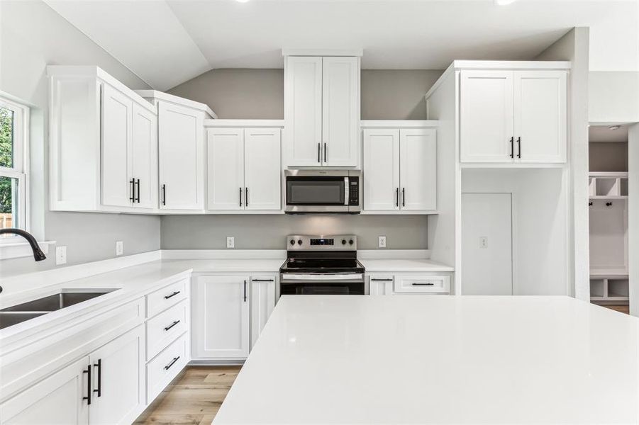 Kitchen with lofted ceiling, sink, appliances with stainless steel finishes, and white cabinets