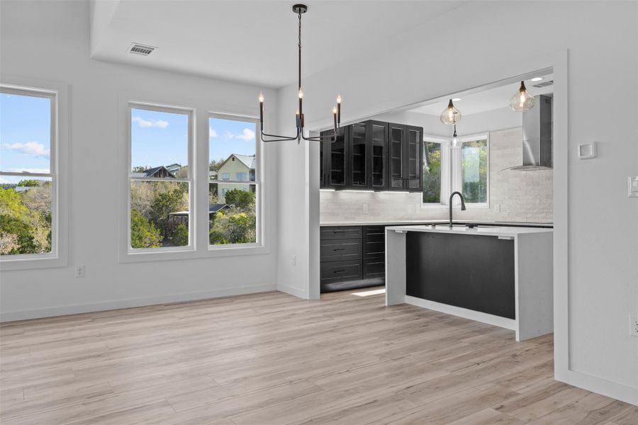 Kitchen featuring glass fronted cabinets, hanging lights, decorative backsplash, light wood-type flooring, and light stone counters