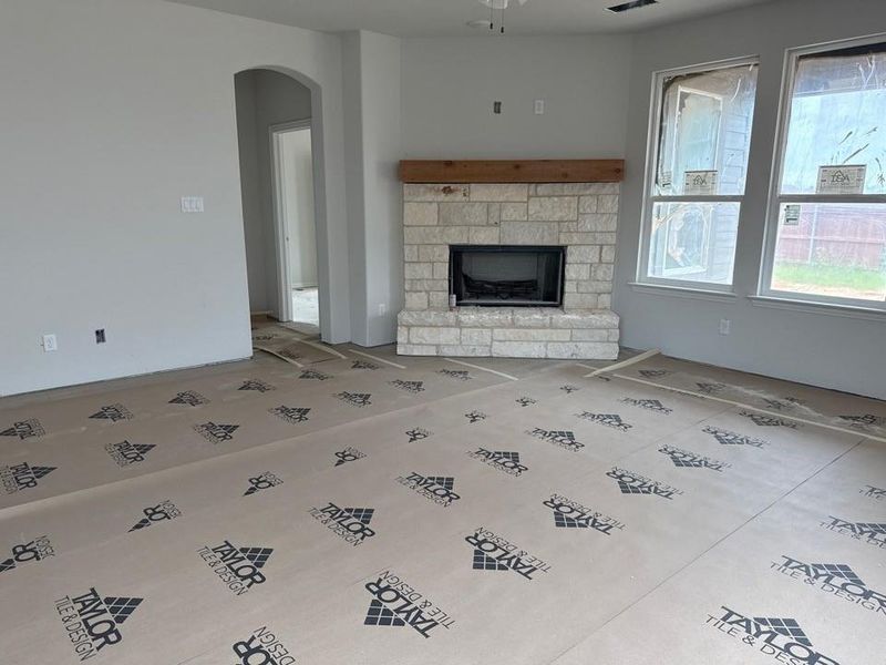 Spacious room featuring a stone-clad fireplace with a wood mantel, multiple large windows providing ample natural light, and an arched doorway