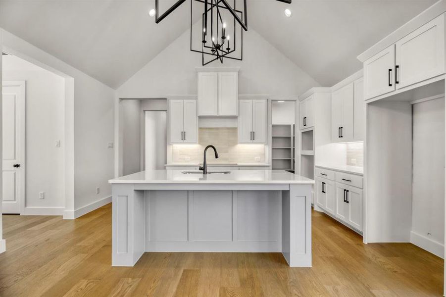Kitchen featuring a high ceiling, white cabinetry, a center island with sink, decorative backsplash, and light wood-style floors