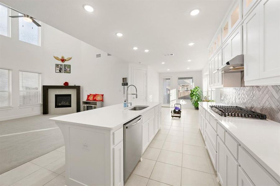 Kitchen with open floor plan, white cabinetry, stainless steel appliances, light tile patterned floors, and glass insert cabinets