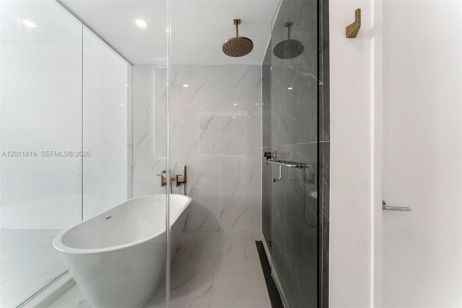 Spa-inspired primary bathroom featuring dual vanities, a deep soaking tub, a frameless glass rainfall shower, and designer porcelain tile throughout.