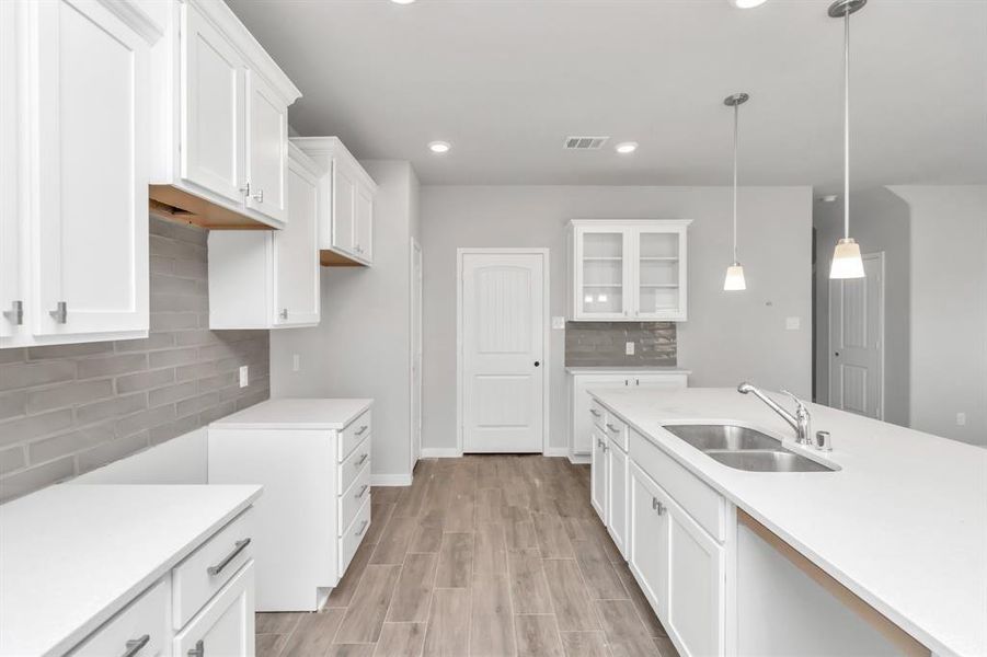 This angle of the kitchen highlights its practical layout and abundant storage options. The white cabinetry, modern backsplash, and spacious countertops create a clean, streamlined look. Whether you're preparing a gourmet meal or enjoying a quick snack, this kitchen is designed to meet all your culinary needs with style and efficiency. **This image is from another Saratoga Home with similar floor plan and finishes, not the June floorplan.**