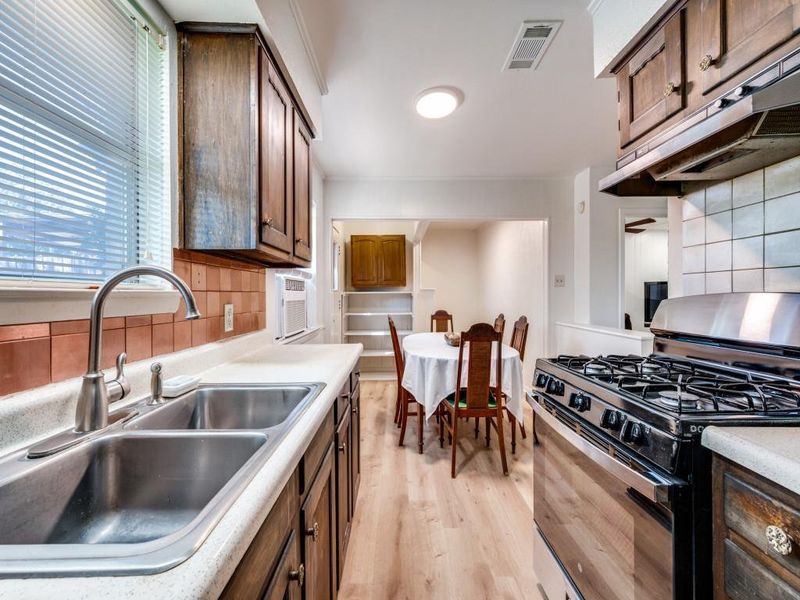 Kitchen with decorative backsplash, stainless steel gas range, light wood-style floors, and under cabinet range hood Kitchen with decorative backsplash, stainless steel gas range, light wood-style floors, and under cabinet range hood