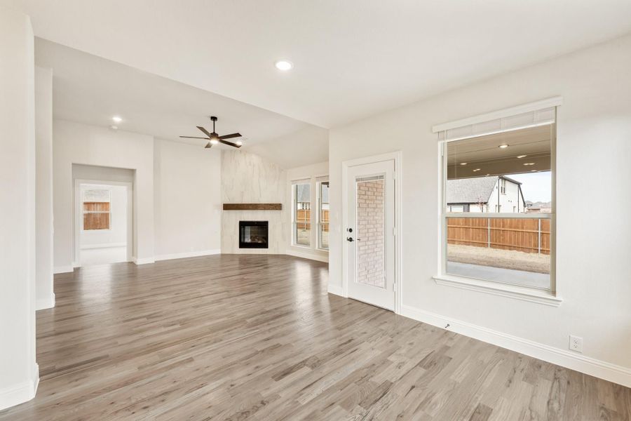 Open living room with hardwood floors, ceiling fan, fireplace, and glass back door leading to covered patio