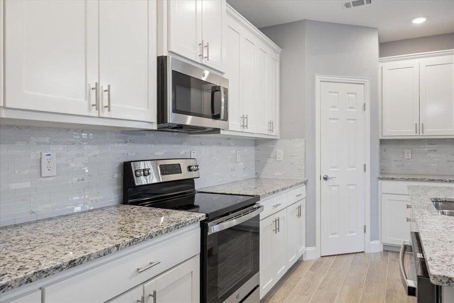 Kitchen featuring light stone countertops, tasteful backsplash, white cabinetry, light wood-type flooring, and stainless steel appliances