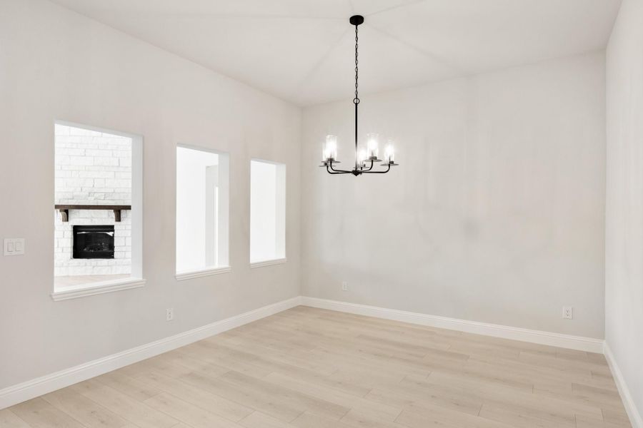 Empty living room with white brick fireplace, black chandelier, and light hardwood floors