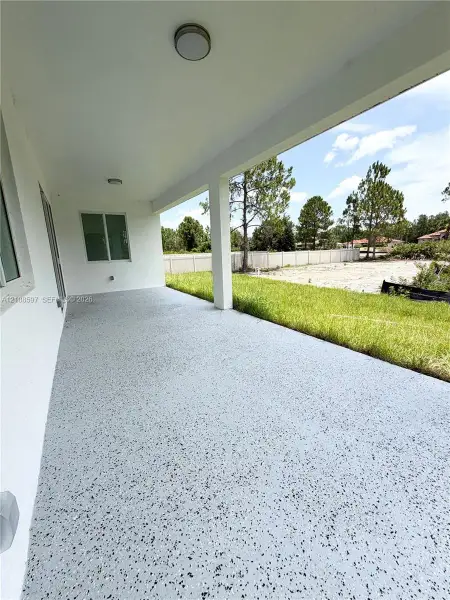 Covered concrete patio featuring a speckled epoxy finish, flush-mount ceiling lighting, and support columns