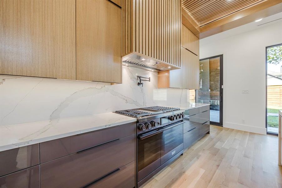 Kitchen with modern cabinets, light stone countertops, black gas stove, premium range hood, and light wood-style flooring Kitchen with modern cabinets, light stone countertops, black gas stove, premium range hood, and light wood-style flooring