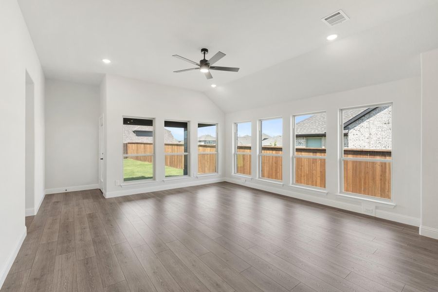 Open living room with vaulted ceiling, ceiling fan, hardwood floors, and large windows overlooking backyard Open living room with vaulted ceiling, ceiling fan, hardwood floors, and large windows overlooking backyard