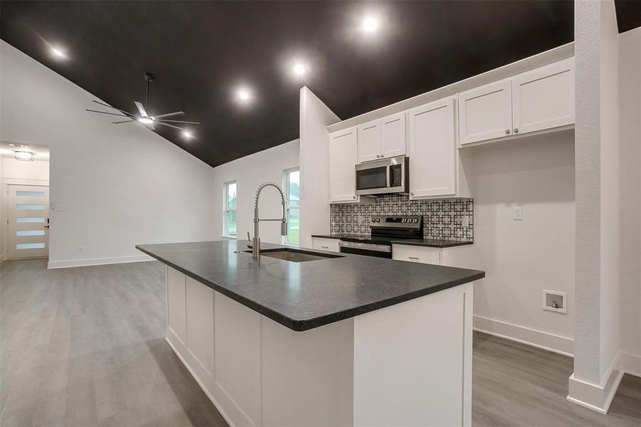 Kitchen with appliances with stainless steel finishes, dark countertops, light wood-type flooring, ceiling fan, and white cabinets