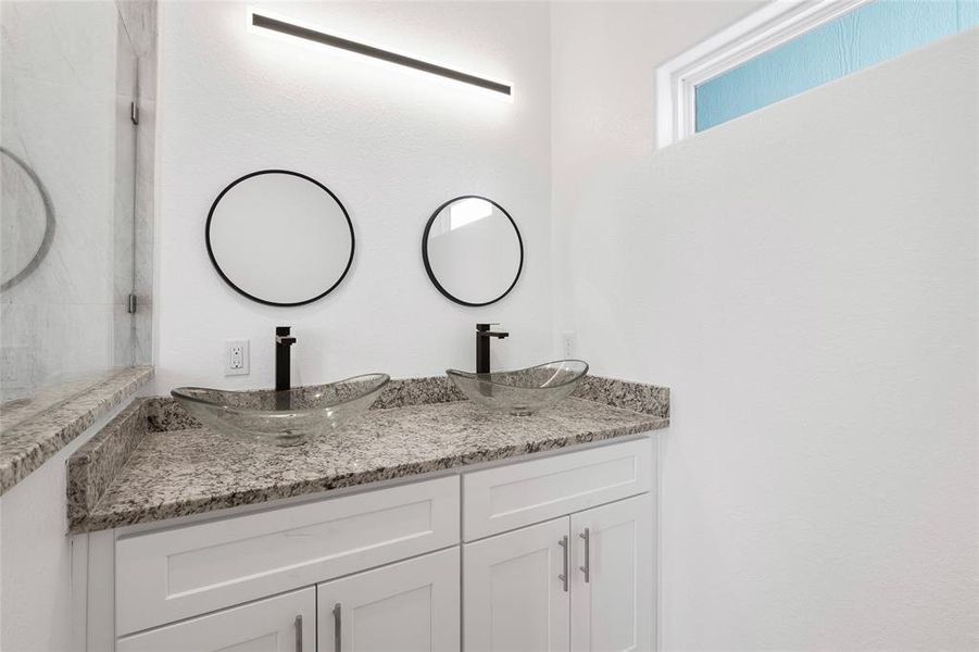 This primary bathroom features  sleek cabinetry, round framed mirrors and a linear light fixture.