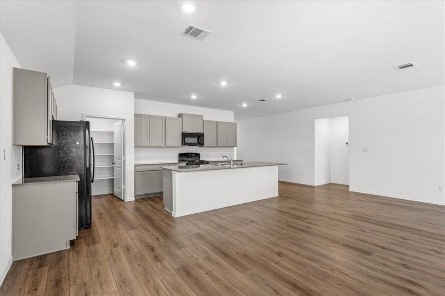 Kitchen with black appliances, gray cabinetry, a kitchen island with sink, light countertops, and dark wood-style floors