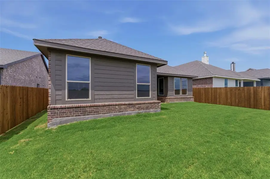 Expansive green lawn surrounds the property, featuring a privacy fence and a brick foundation
