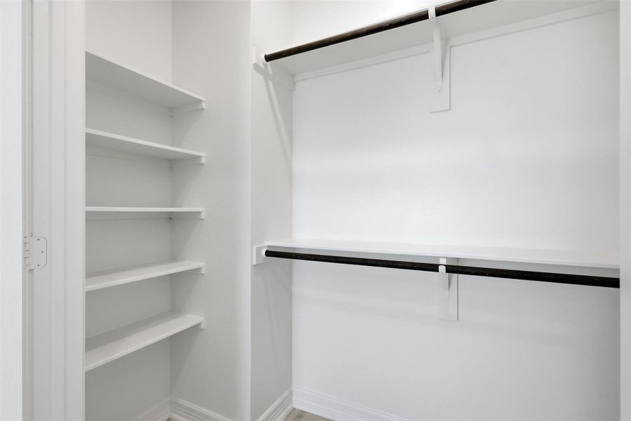 Spacious walk in closet with custom built in shelving, organized storage sections, and ample space.