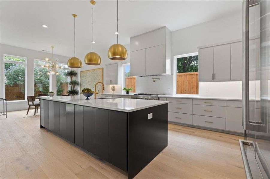 Kitchen with light hardwood / wood-style floors, a large island with sink, hanging light fixtures, and sink