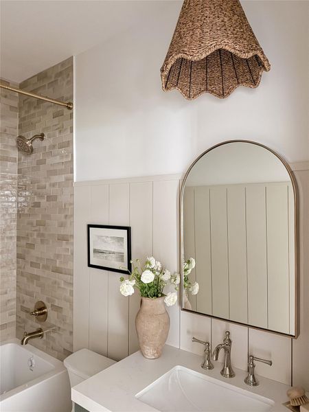 Hall Bathroom featuring designer lighting, wood-finish wall paneling, a circular mirror with a metal frame, and a quartz vanity with an integrated sink and brass faucet Hall Bathroom featuring designer lighting, wood-finish wall paneling, a circular mirror with a metal frame, and a quartz vanity with an integrated sink and brass faucet