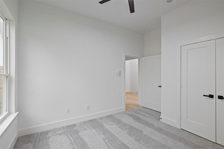 Unfurnished bedroom with light colored carpet, multiple windows, and ceiling fan