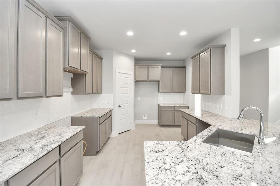 This spacious kitchen features high ceilings, dark stained wood cabinets, granite countertop, SS appliances, modern tile backsplash, recessed lighting, extended counter space, and a walk-in pantry all overlooking your huge family room.