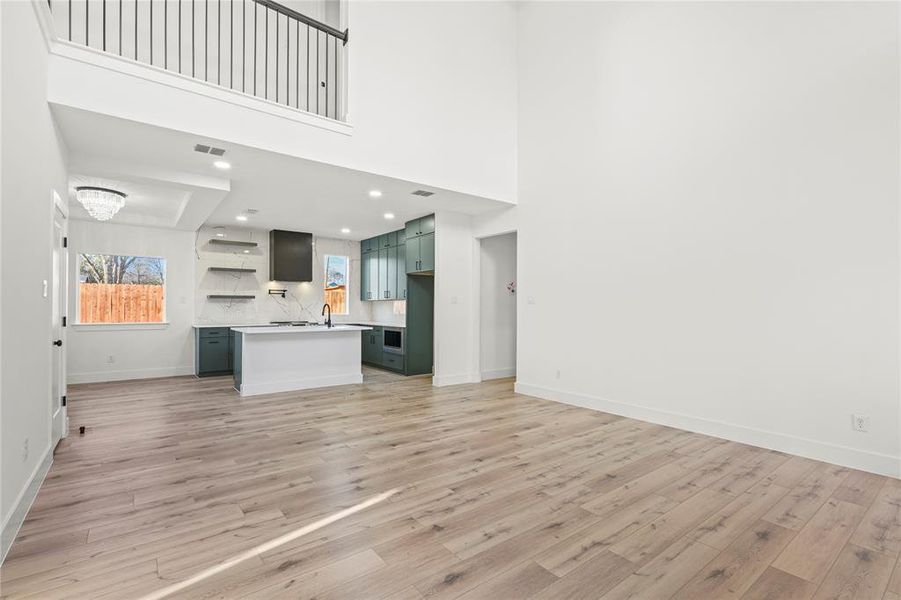 Unfurnished living room with recessed lighting, light wood-style floors, a chandelier, and a high ceiling