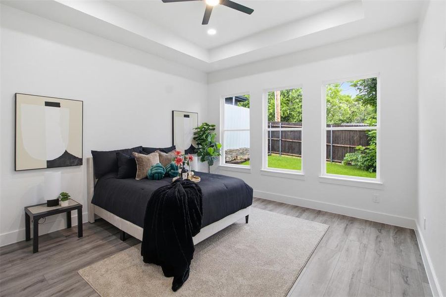 Bedroom featuring a tray ceiling with a ceiling fan, light wood-finish flooring, and multiple windows