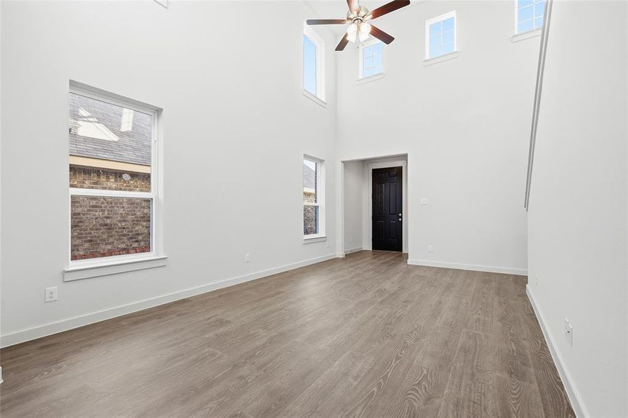 Spacious interior with soaring ceilings, wood-finish flooring, multiple windows, and a ceiling fan Spacious interior with soaring ceilings, wood-finish flooring, multiple windows, and a ceiling fan