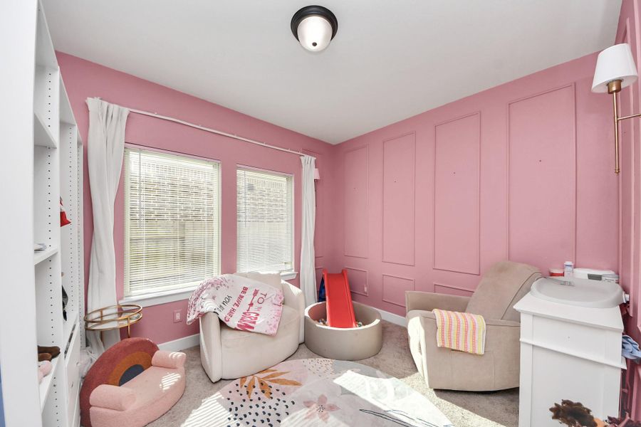 This cozy room features pink walls with decorative paneling, two large windows with white curtains, and soft carpet flooring. It's furnished with a comfortable armchair, a small slide, and a changing table, making it ideal for a child's nursery or playroom. This cozy room features pink walls with decorative paneling, two large windows with white curtains, and soft carpet flooring. It's furnished with a comfortable armchair, a small slide, and a changing table, making it ideal for a child's nursery or playroom.