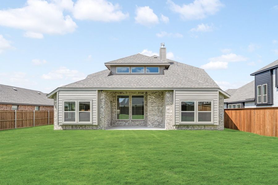 Rear exterior of single-story brick home with covered patio, large windows, and fenced backyard with green lawn.